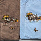Two folded shirts, one brown and one blue, with embroidered designs of a highland cow and sunflowers.